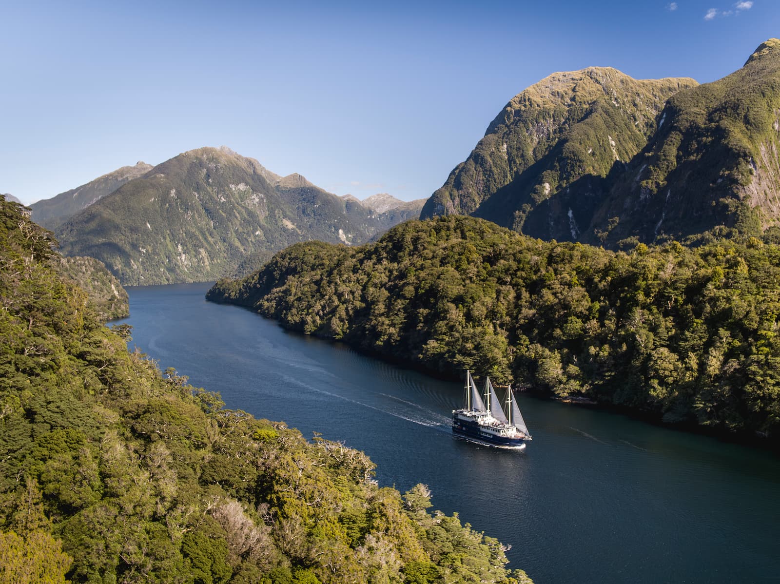 Aerial view of overnight cruise boat sailing through Doubtful Sound surrounded by native forest Fiordland New Zealand
