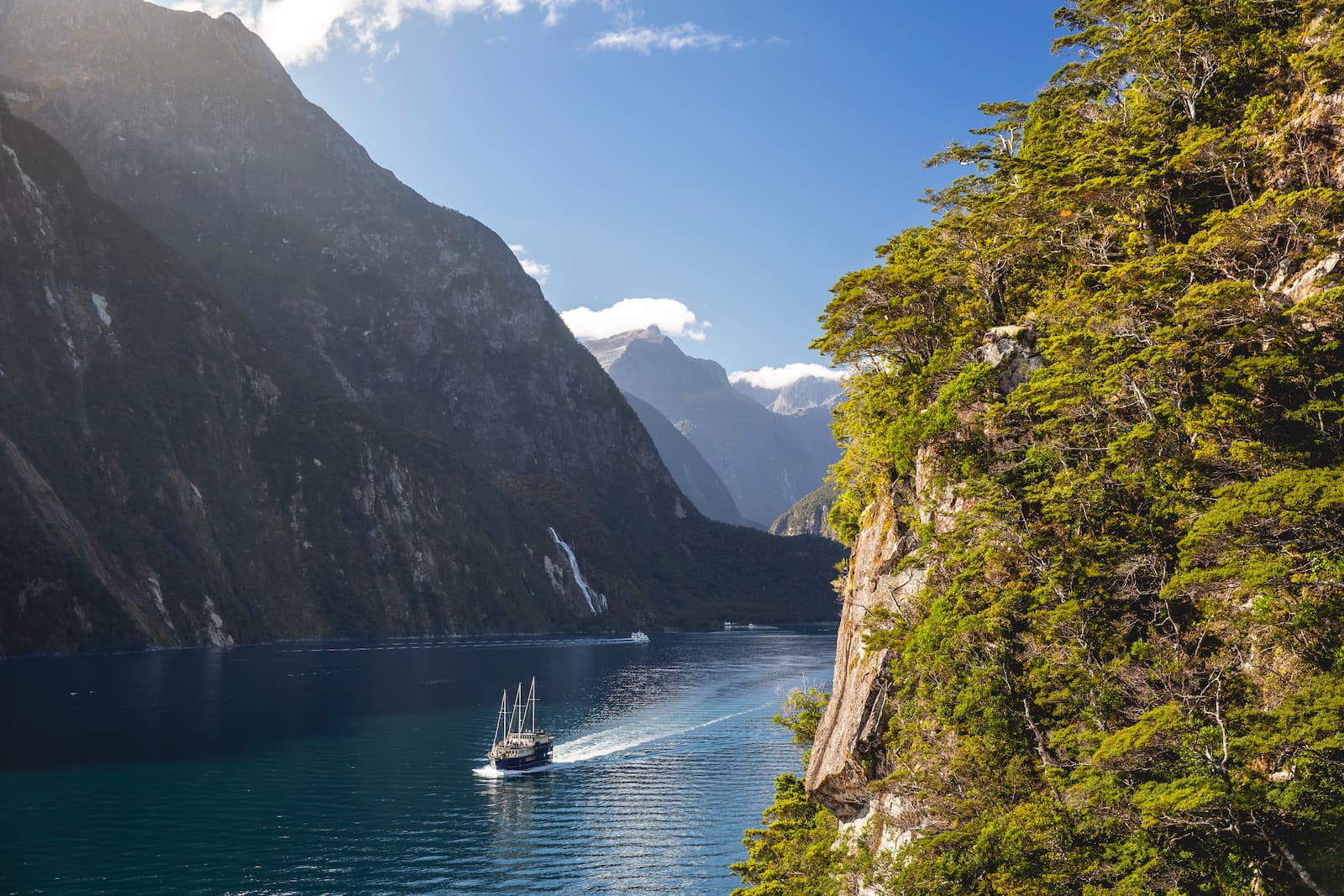 Cruise boat sailing through Milford Sound fiord with towering cliffs and native bush Fiordland New Zealand